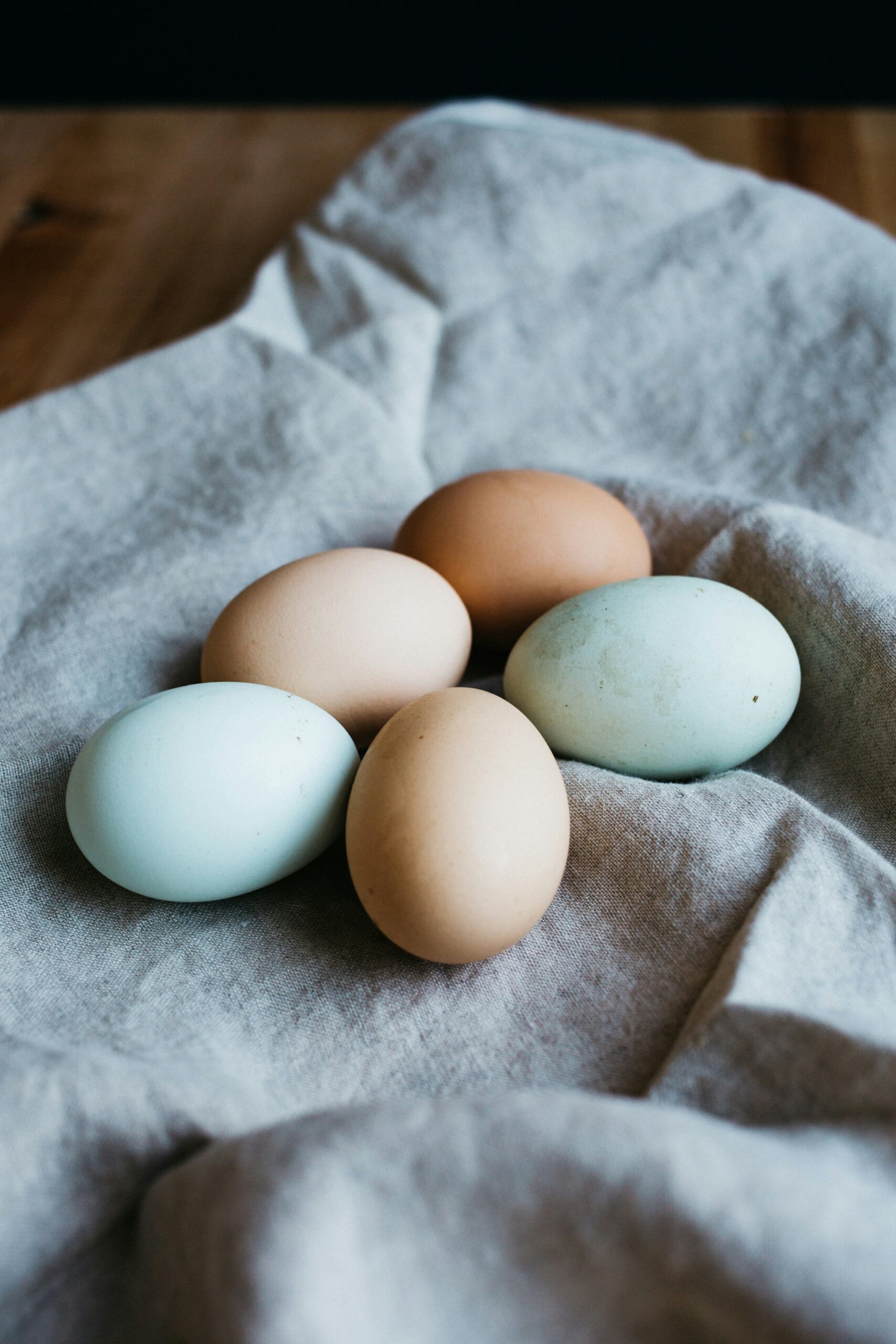 A collection of five colorful eggs, including brown and blue varieties, arranged on a soft linen cloth, showcasing natural textures and hues for a rustic kitchen setting.